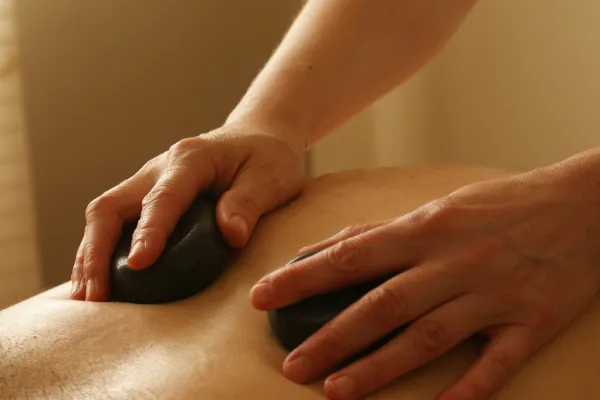 Two hands holding a black color hot stones massaging the back.